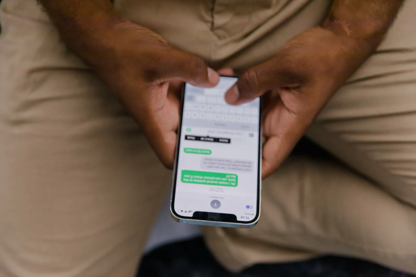 A person holding an iPhone showing a green-bubble SMS conversation, illustrating that Twilio sends SMS rather than blue-bubble iMessage