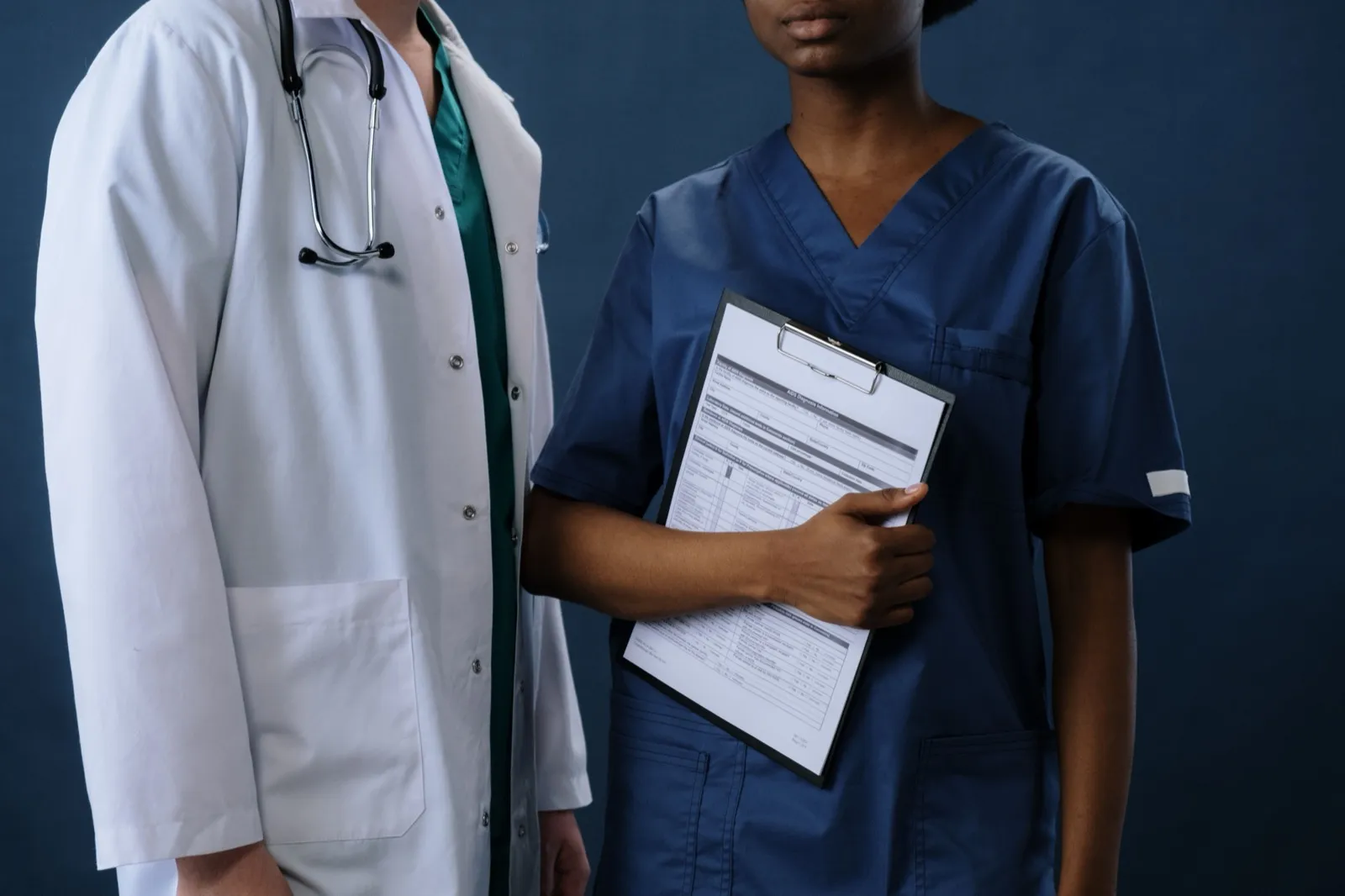 A doctor with a stethoscope and a nurse holding a patient record on a clipboard, representing HIPAA and patient data privacy in messaging